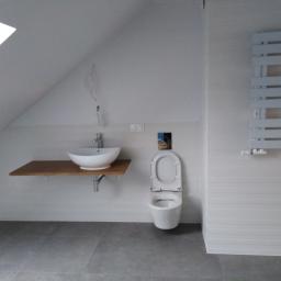 Onsetbud Zhanna Slyvka - Ukończona łazienka na poddaszu ze skośnym sufitem, umywalka nablatowa na drewnianym blacie, wisząca toaleta i grzejnik drabinkowy.
