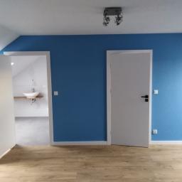 Onsetbud Zhanna Slyvka - Pokój na poddaszu z niebieską ścianą, drewnianą podłogą i otwartymi białymi drzwiami do łazienki z umywalką na drewnianym blacie.