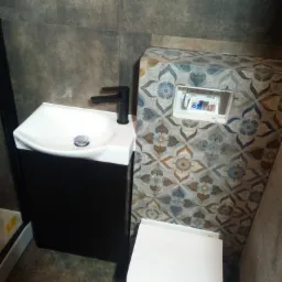 Nowoczesna łazienka z umywalką nablatową na czarnej szafce, toaletą wiszącą z ozdobną obudową i szarą płytką na ścianach.