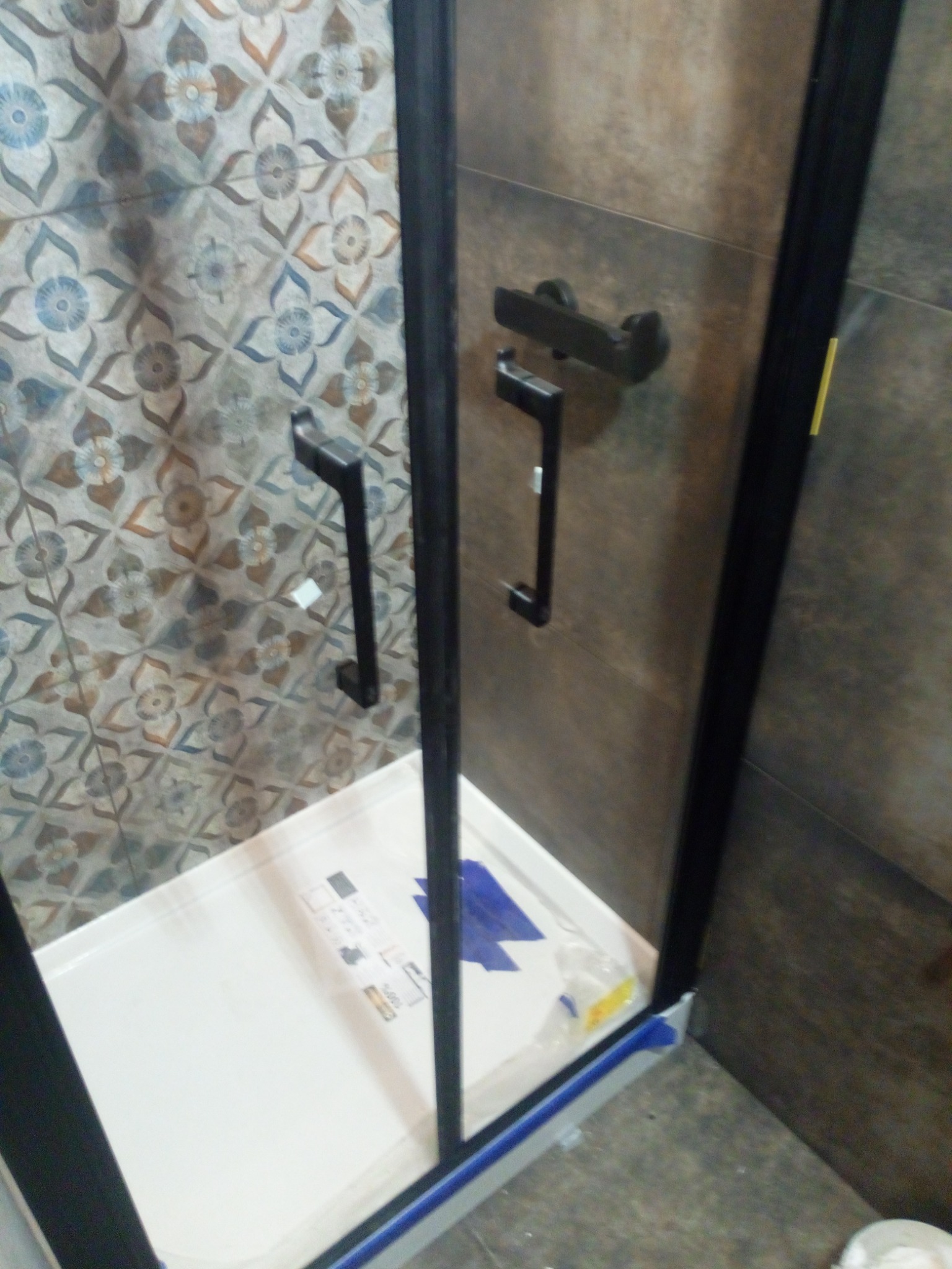 Nowoczesna kabina prysznicowa z czarnymi profilami i uchwytami, widok na brodzik i wzorzyste płytki ścienne