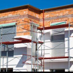 Przemo - Niedokończony budynek z czerwonej cegły i białego styropianu, częściowo osłonięty rusztowaniem, okna zasłonięte roletami.