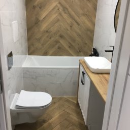 Przemo - Nowoczesna łazienka z drewnopodobną okładziną w jodełkę na podłodze i ścianie, biała armatura i umywalka nablatowa na drewnianym blacie.