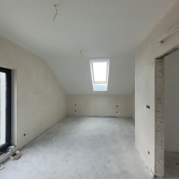 Spec Tynk Paweł Zawrotny - Poddasze w stanie deweloperskim z oknem dachowym, ściany częściowo pokryte tynkiem, widoczne instalacje elektryczne, surowa posadzka.