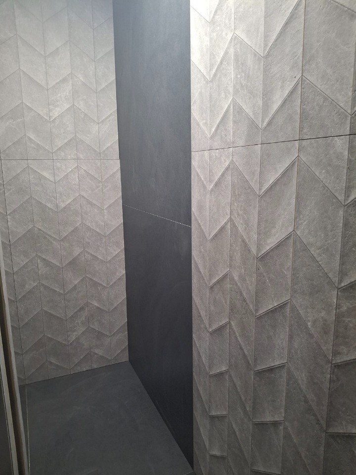 Wykończona łazienka z szarymi płytkami w jodełkę na ścianach i ciemnoszarą ścianą. Minimalistyczny design, nowoczesne wykończenie, kątowe ujęcie.