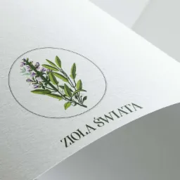 Logo firmy 'Zioła Świata' z rysunkiem gałązki szałwii w okręgu, wydrukowane na białym, fakturowanym papierze, widoczne pod kątem.