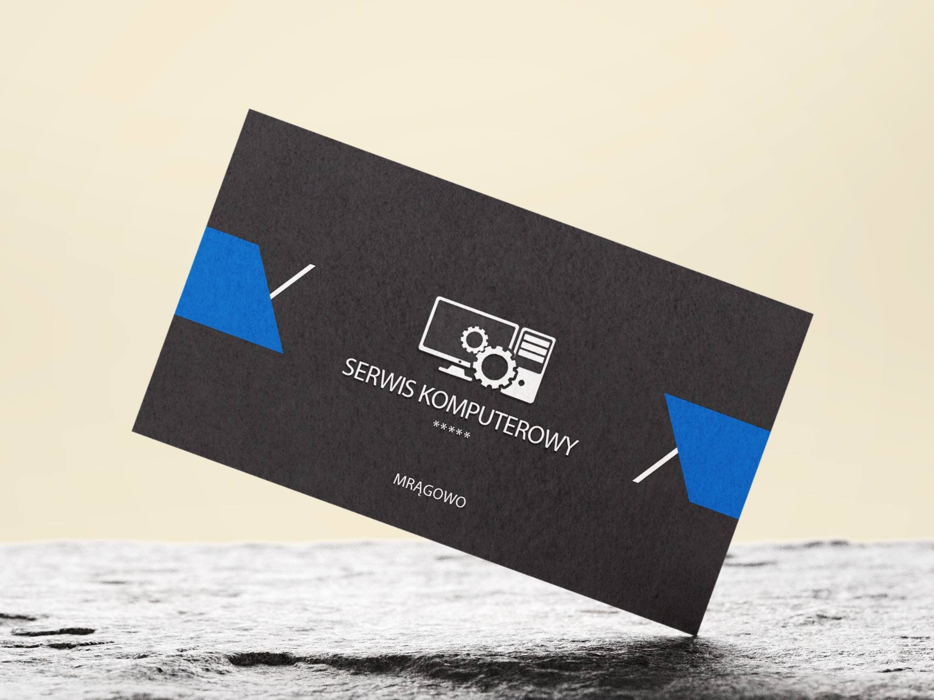 Czarna wizytówka z niebieskimi akcentami i białym logo przedstawiającym komputer z kołami zębatymi, leżąca na szarej, teksturowanej powierzchni.