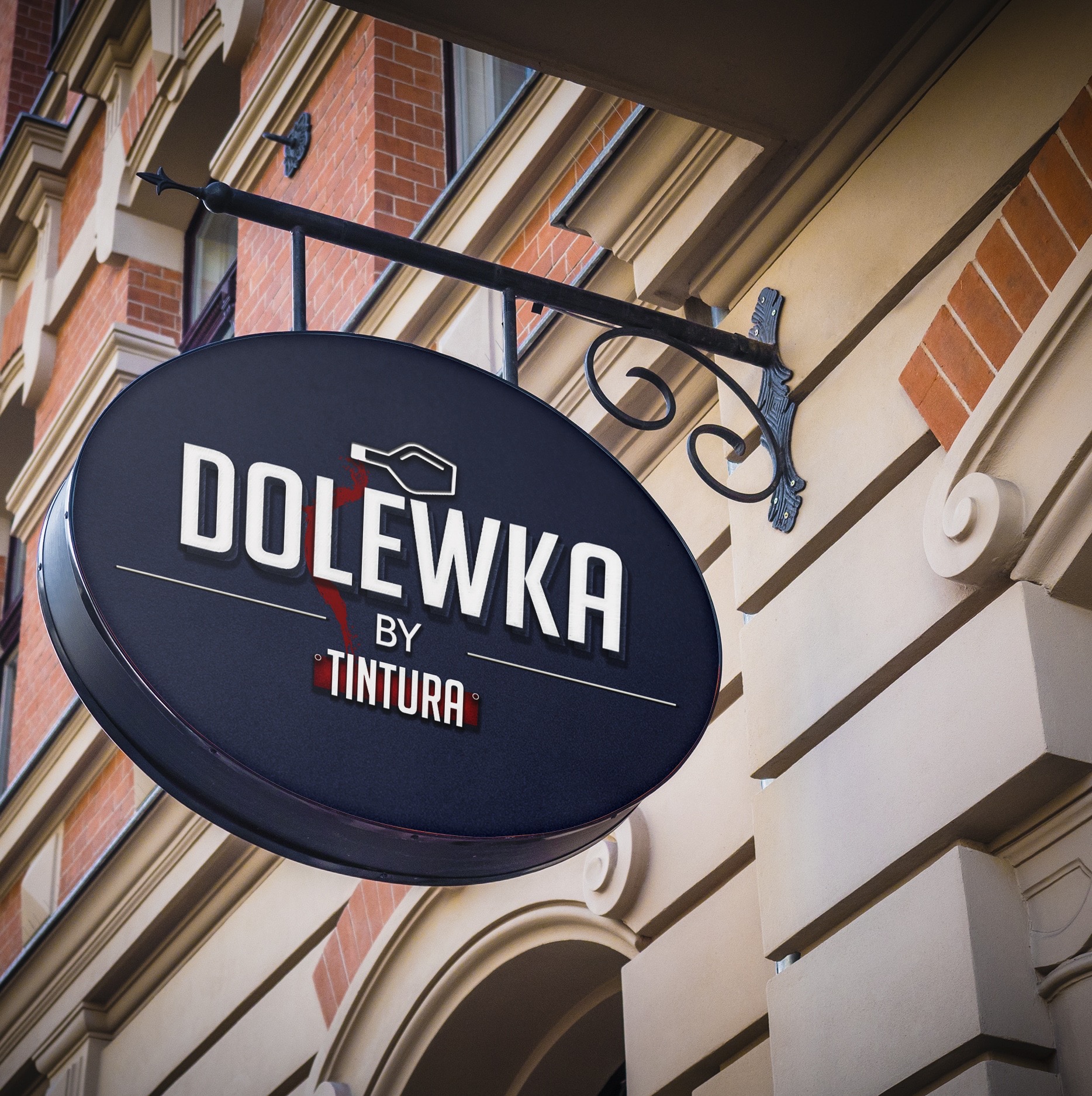 Elegancki, okrągły szyld z nazwą 'DOLEWKA by TINTURA' zawieszony na ozdobnym, kutym uchwycie na elewacji budynku z cegły i piaskowca.