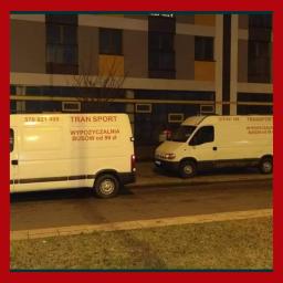 Sebastian Gągol - Dwa białe busy z napisem 'WYPOŻYCZALNIA BUSÓW od 99 zł' zaparkowane na tle budynku mieszkalnego o zmierzchu.