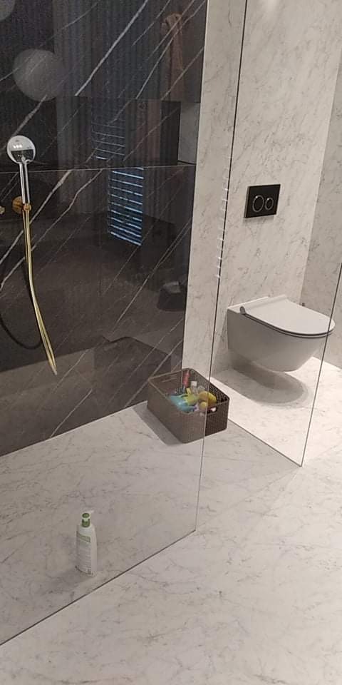 Nowoczesna łazienka z czarnymi marmurowymi płytkami pod prysznicem, białymi marmurowymi płytkami na ścianie, wiszącą toaletą i szklaną kabiną prysznicową.