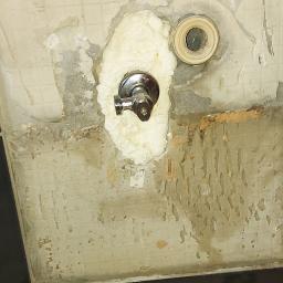 Hydra-luk - Niedokończona ściana w łazience z zamontowanym, chromowanym zaworem i fragmentem rury, otoczonymi pianką montażową; widoczne fragmenty starej glazury i gruz po remoncie.