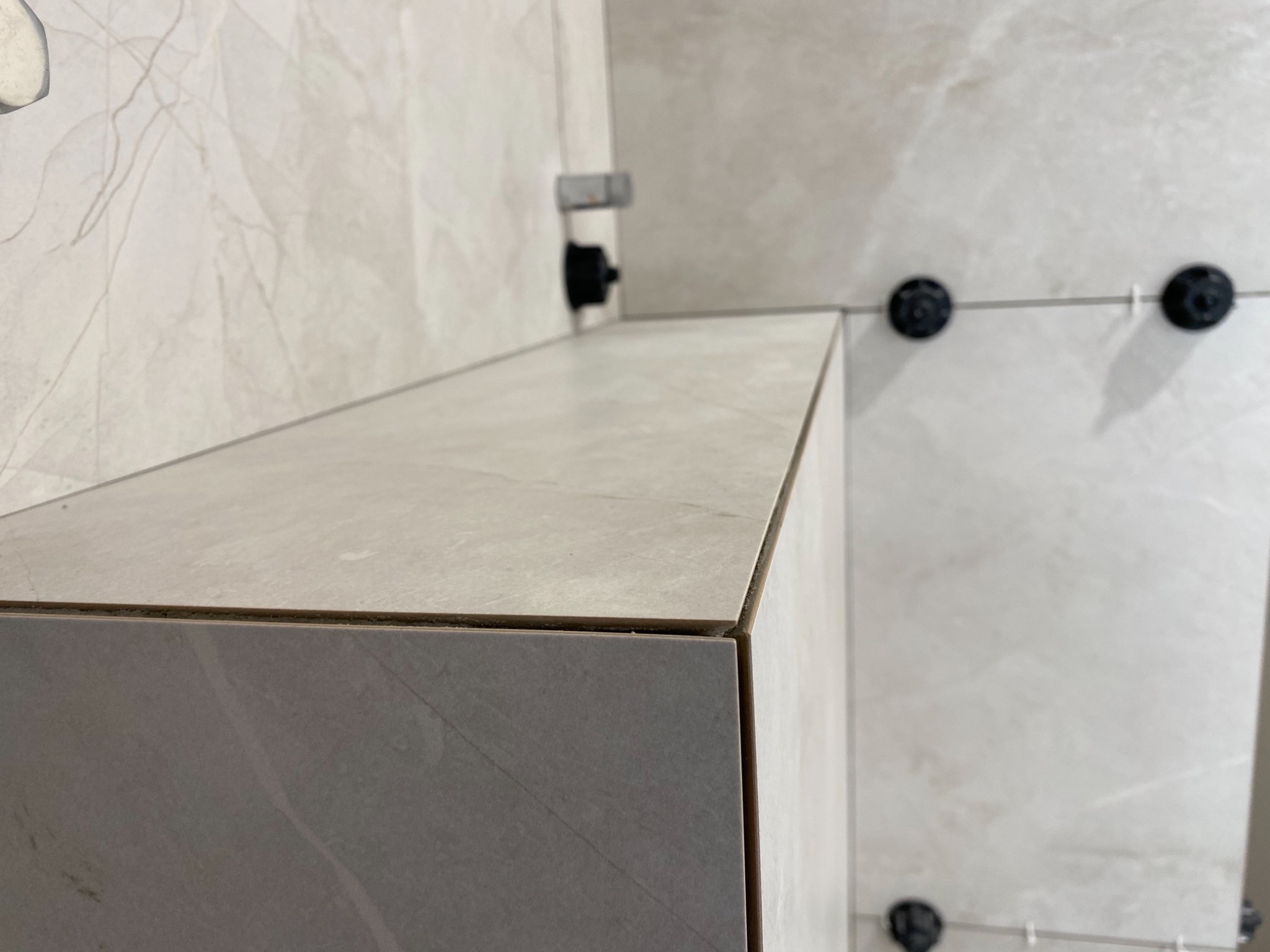 Fragment ściany i zabudowy z płytek imitujących marmur w trakcie montażu w Warszawie, widoczne czarne klipsy poziomujące płytki.