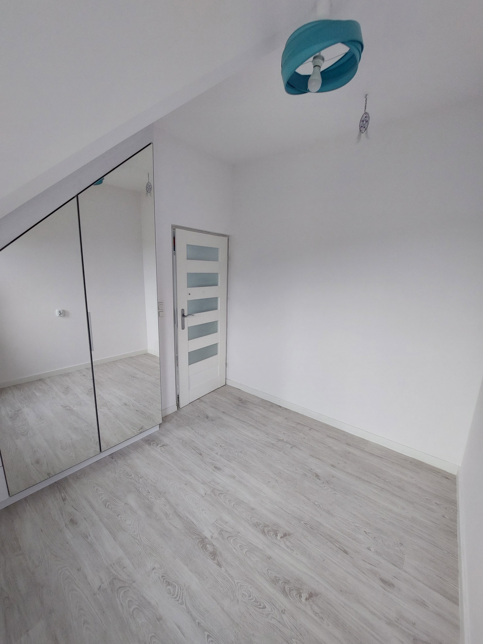 Poddasze po remoncie: białe ściany, laminowana podłoga w odcieniach szarości, białe drzwi z przeszkleniami i szafa z lustrzanymi drzwiami.