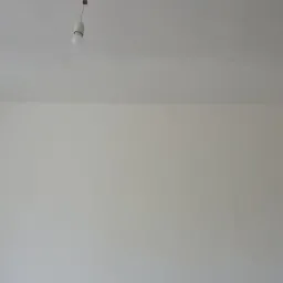 Świeżo pomalowane ściany na biało w pokoju w Zielonej Górze, widoczna wisząca żarówka i fragment kartonu oparty o ścianę.