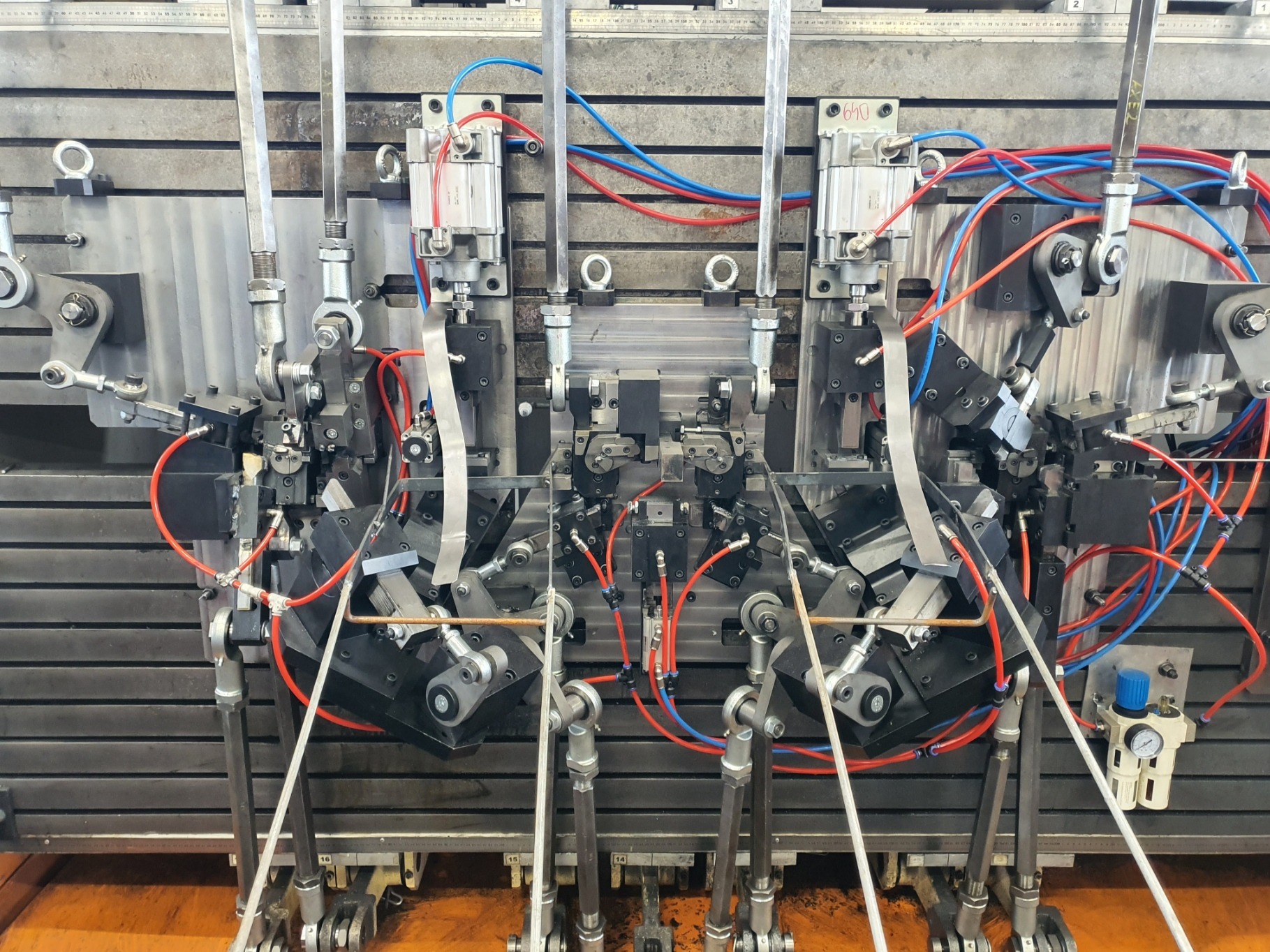 Precyzyjna maszyna do obróbki metalu z licznymi przewodami i elementami hydraulicznymi, ustawiona na metalowej płycie z widocznymi śladami użytkowania.