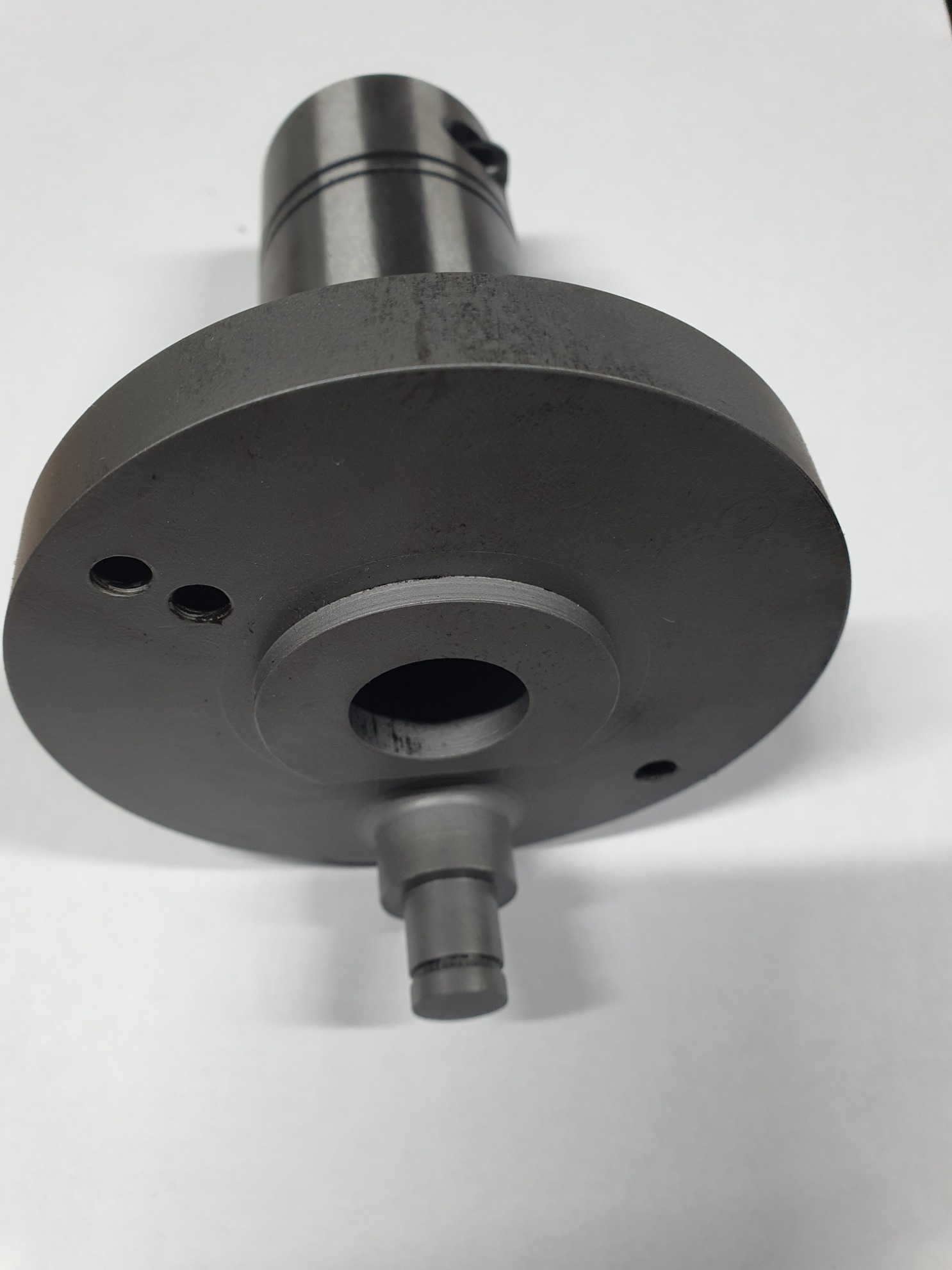 Szary, metalowy element tokarski z otworem centralnym i bocznymi, widoczny z bliska na białym tle. Precyzyjna obróbka, detal przemysłowy.