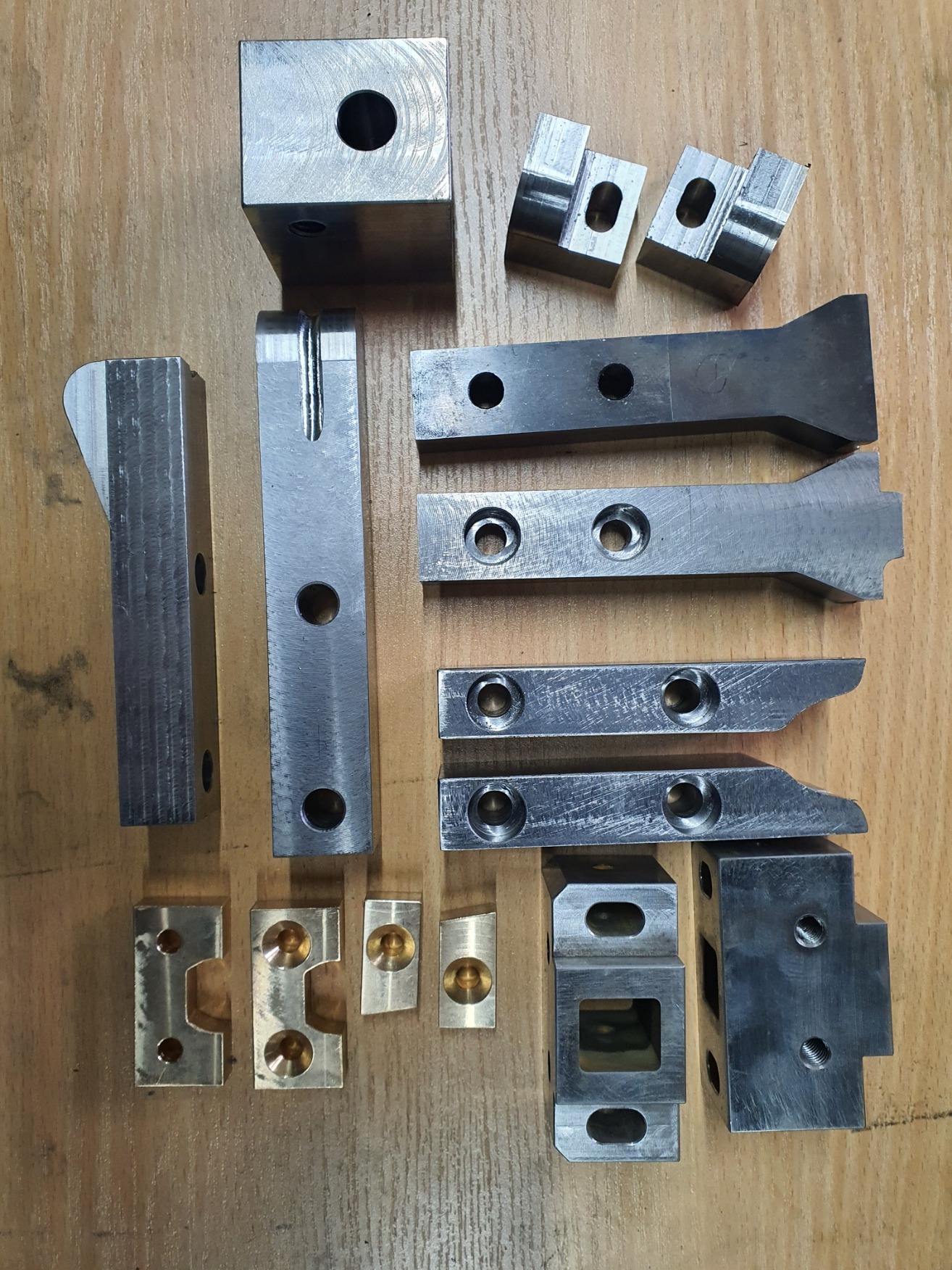 Metalowe elementy po obróbce skrawaniem z widocznymi otworami i rowkami, ułożone na drewnianym blacie w Gorzowie. Różne kształty i rozmiary, detale precyzyjnie wykonane.