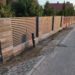 Nowoczesne ogrodzenie panelowe z betonowymi słupkami i poziomymi przęsłami, widok z boku na tle zieleni i domów.