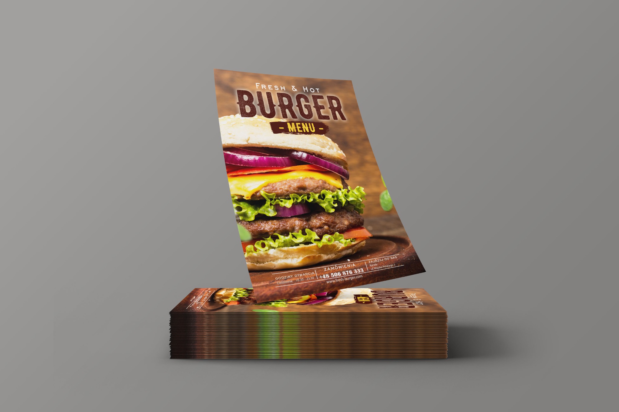 Stos ulotek z grafiką burgera, jedna ulotka unosi się nad stosem, prezentując menu restauracji z godzinami otwarcia i numerem telefonu.