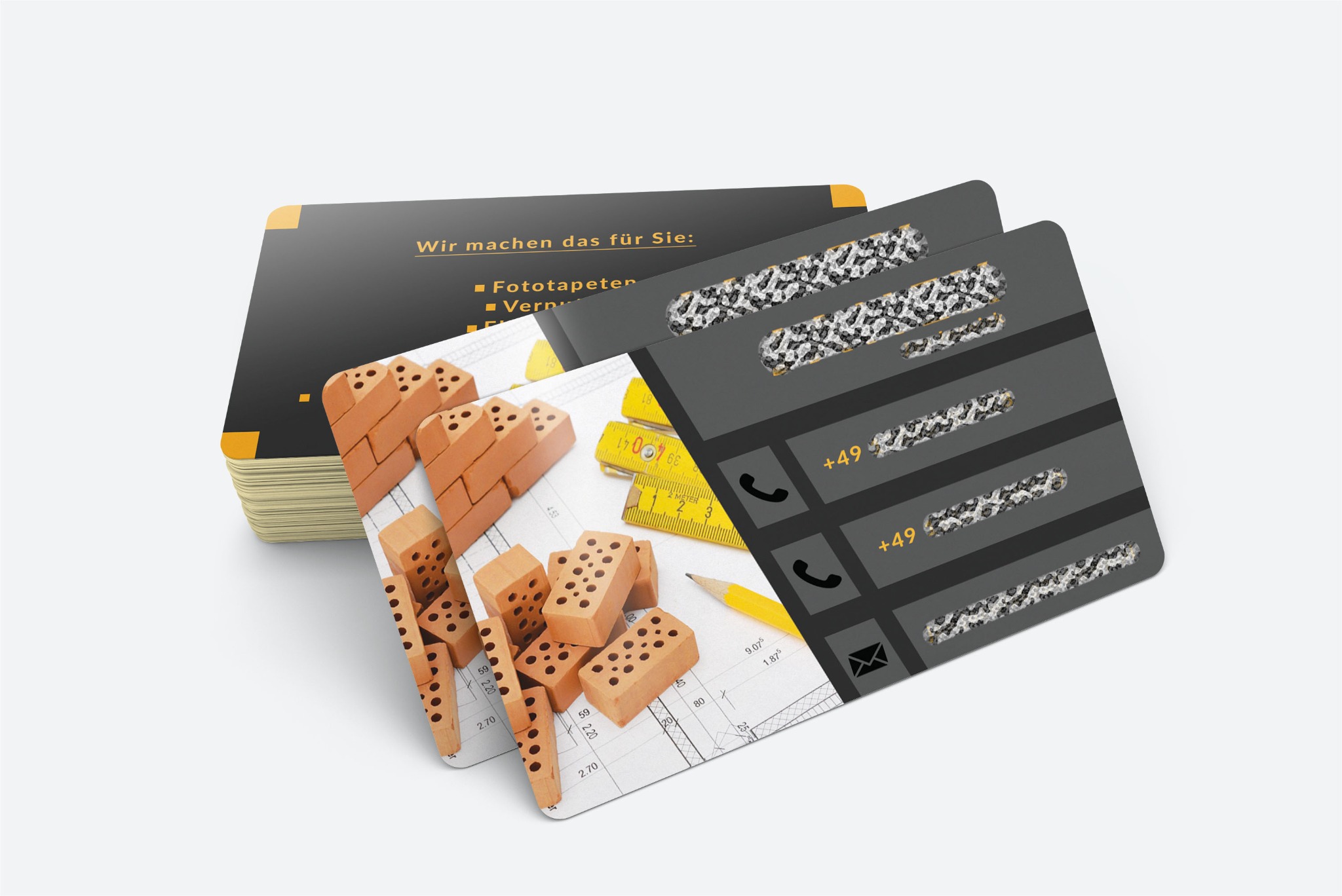 Stos wizytówek z zaokrąglonymi rogami, przedstawiających projekt budowlany z cegłami, miarką i ołówkiem, oraz dane kontaktowe z numerami telefonów i adresem e-mail.