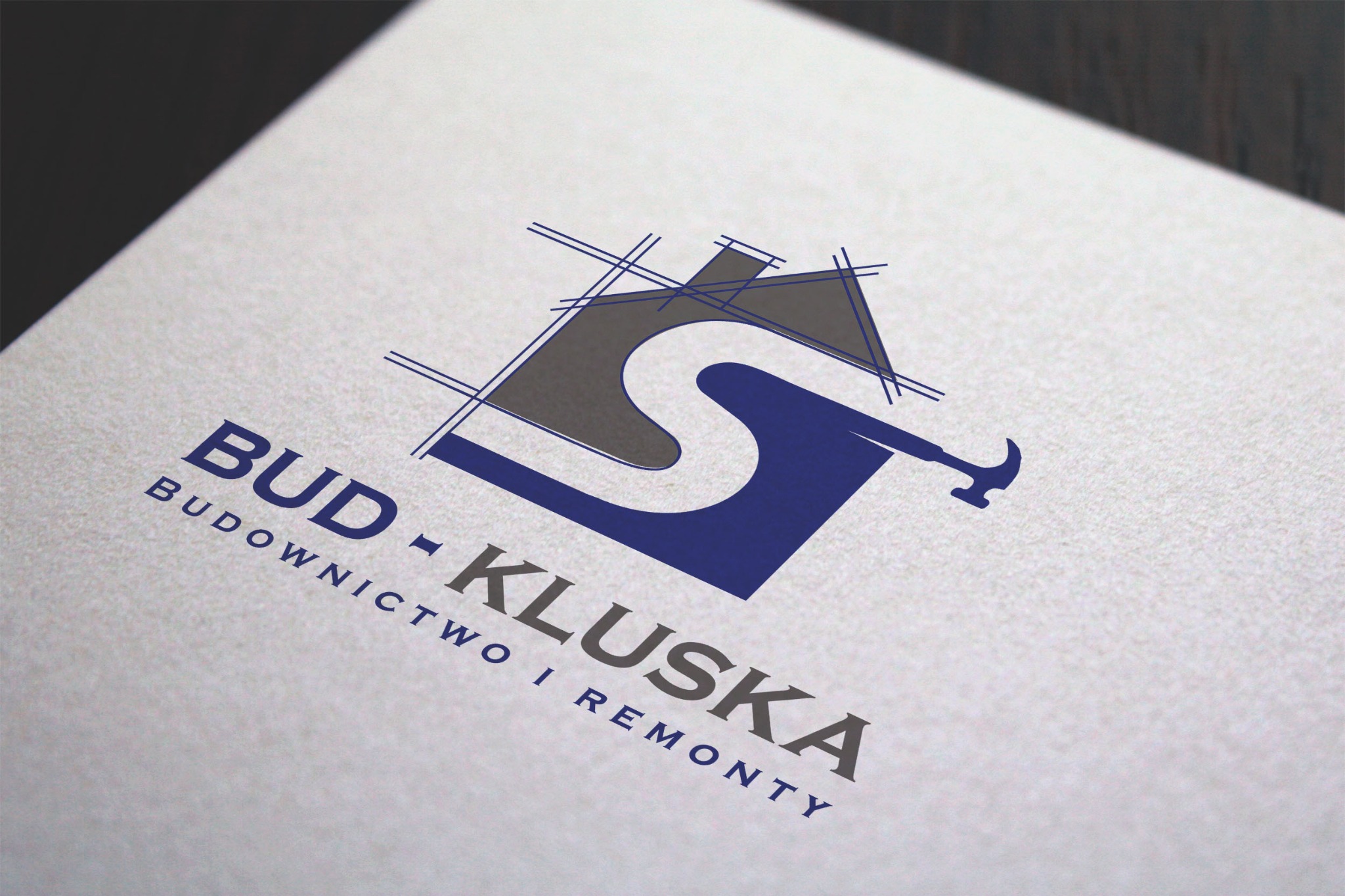 Projekt logo firmy budowlanej 'Bud-Kluska' z motywem domu, litery S i młotka, na teksturowanym papierze.