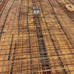 Zbrojenie stropu na deskowaniu, widoczne buty robotnika w dolnej części kadru, w tle zabudowa jednorodzinna.