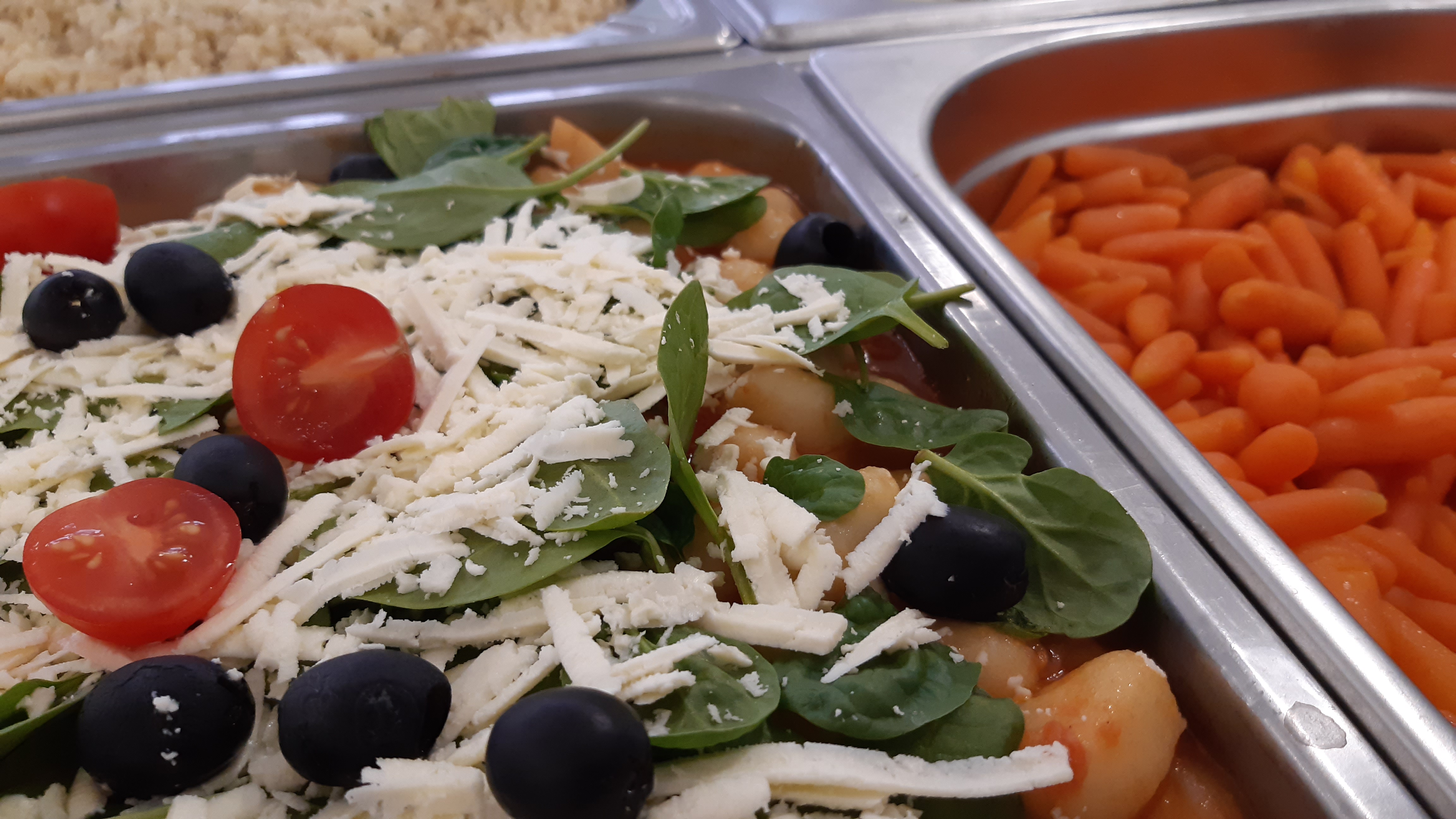 Bufet cateringowy: sałatka z pomidorkami cherry, oliwkami, szpinakiem i serem feta w sosie pomidorowym, obok marchewki baby.