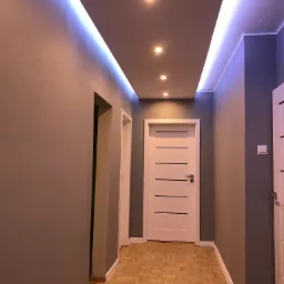 Korytarz z parkietem, oświetleniem LED w suficie podwieszanym i białymi drzwiami z poziomymi frezami.