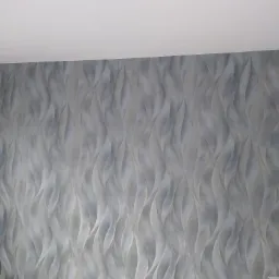 Ściana pokryta dekoracyjną, szarą farbą o falującym wzorze, imitującym płynne linie i subtelne cieniowanie.