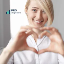 Uśmiechnięta blondynka w białej koszuli formuje dłońmi kształt serca, w tle logo firmy ubezpieczeniowej.