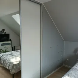 Szafa przesuwna z lustrzanymi drzwiami w pokoju na poddaszu, odbicie okna dachowego, szara ściana ze schowkami i gwiazdkami, drewniana podłoga.