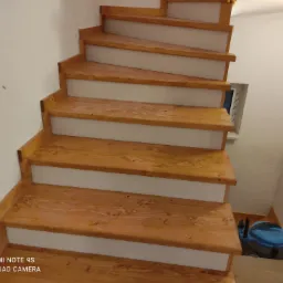 Drewniane schody z jasnymi podstopnicami, widoczne z dołu, z odkurzaczem przemysłowym na podeście.