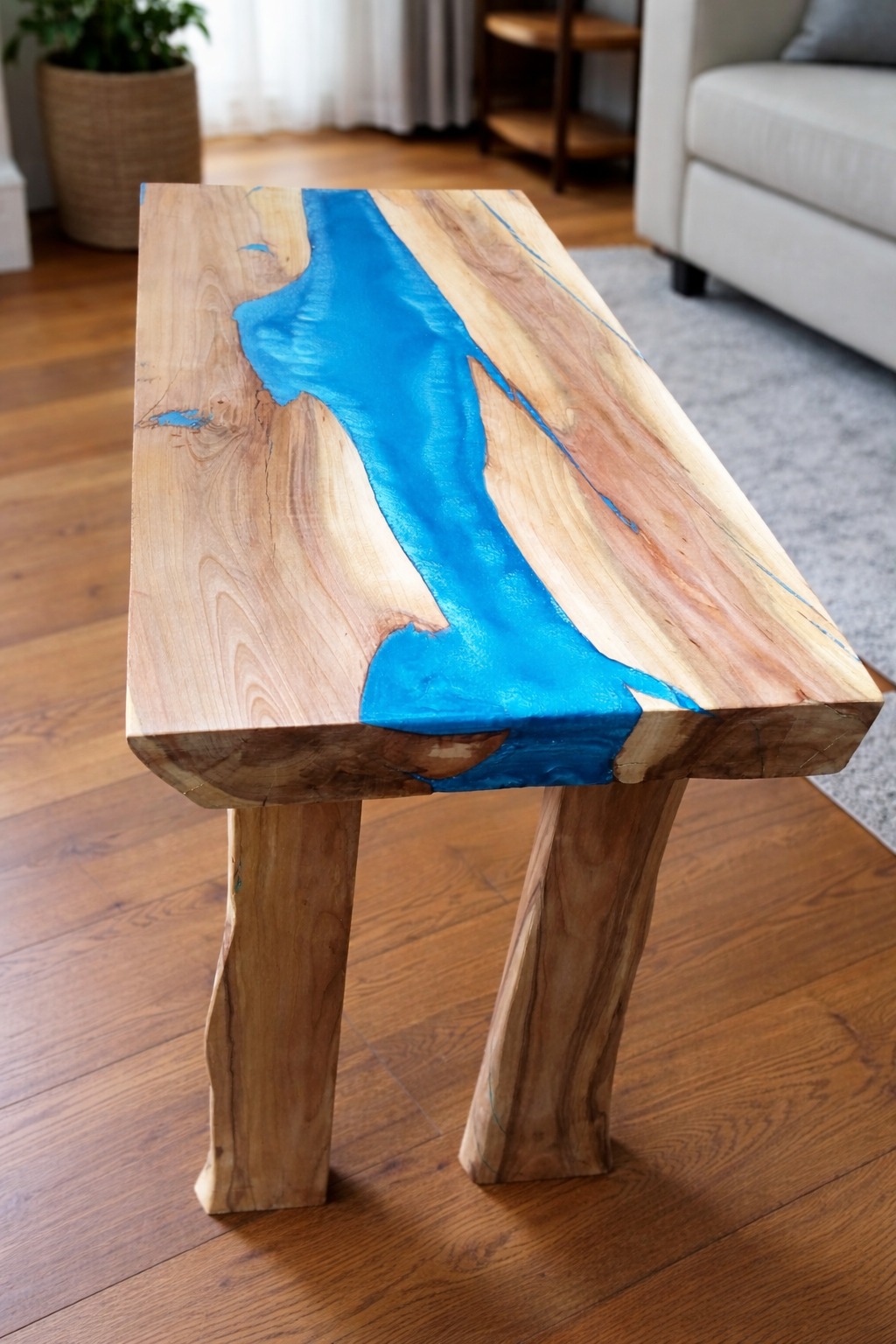 Niski stolik kawowy z blatem z drewna i żywicy epoksydowej w odcieniach błękitu, na dwóch nogach z surowego drewna. Widoczne usłojenie drewna i detale wykończenia.