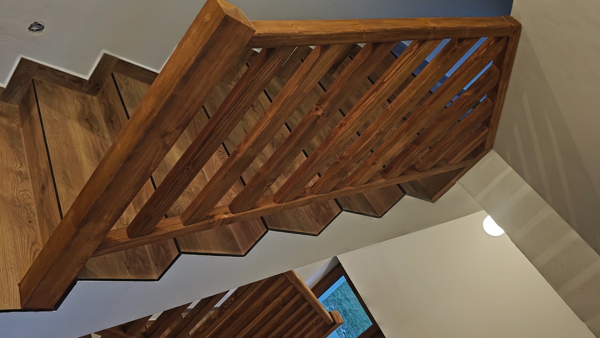 Drewniane schody z balustradą, widok z góry, ukazujący detale wykończenia i naturalny odcień drewna. Ujęcie podkreśla solidność konstrukcji i estetykę wykonania.