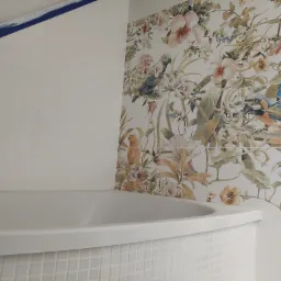 Biała wanna obłożona mozaiką w łazience z płytkami w kwiaty i papugi, zabezpieczone taśmą malarską przy suficie i narożniku