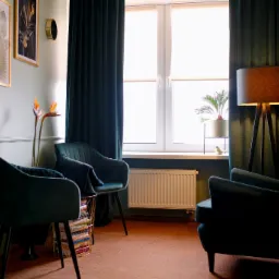 Wnętrze gabinetu z dwoma welurowymi fotelami w odcieniach zieleni, lampą stojącą na trójnogu, obrazami na ścianie i kwiatem strelicji królewskiej w wazonie.