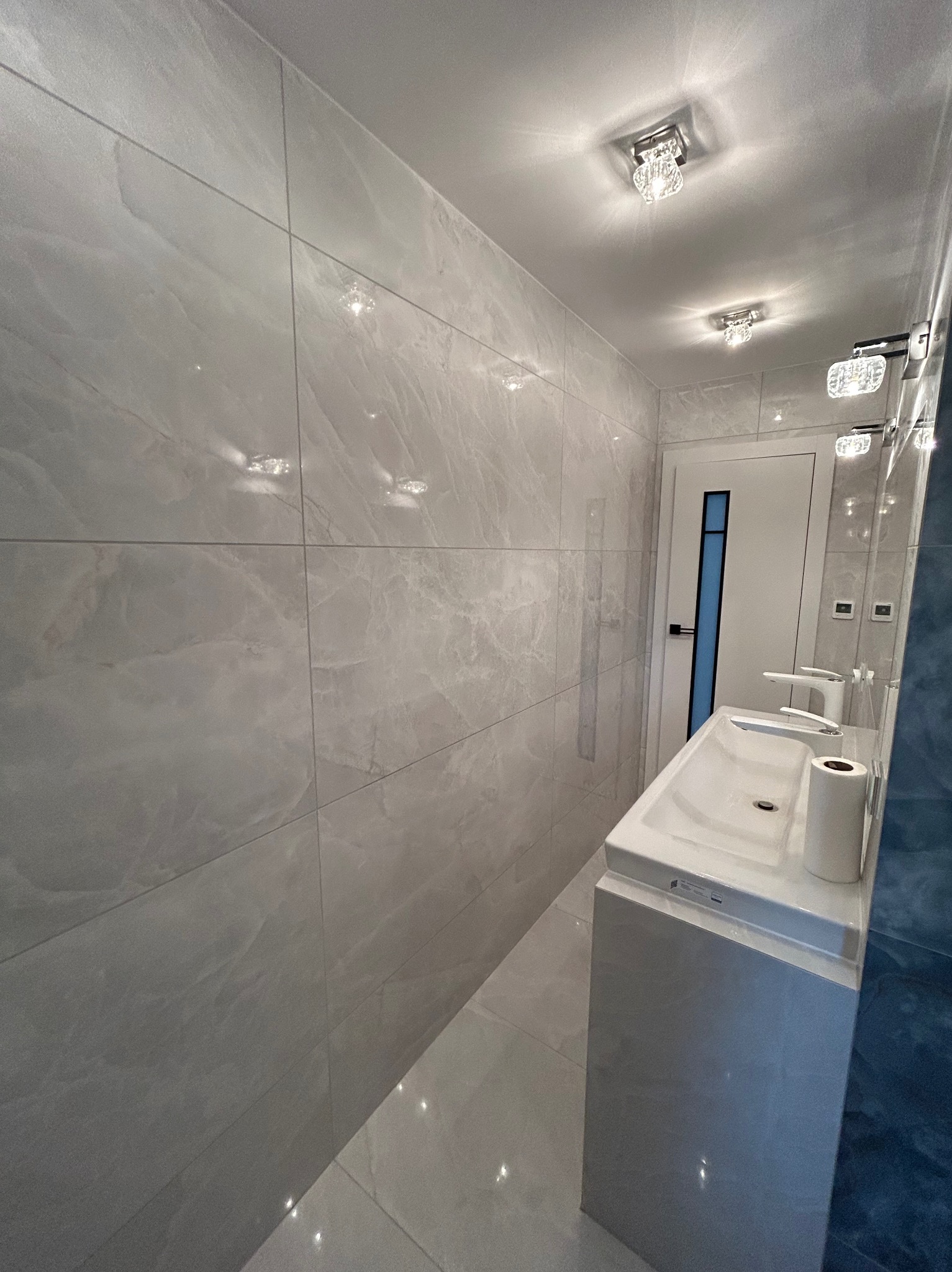 Wykończona łazienka w Łodzi z szarymi płytkami imitującymi marmur na ścianach i podłodze, biała umywalka nablatowa z dwoma kranami i designerskimi lampami sufitowymi.