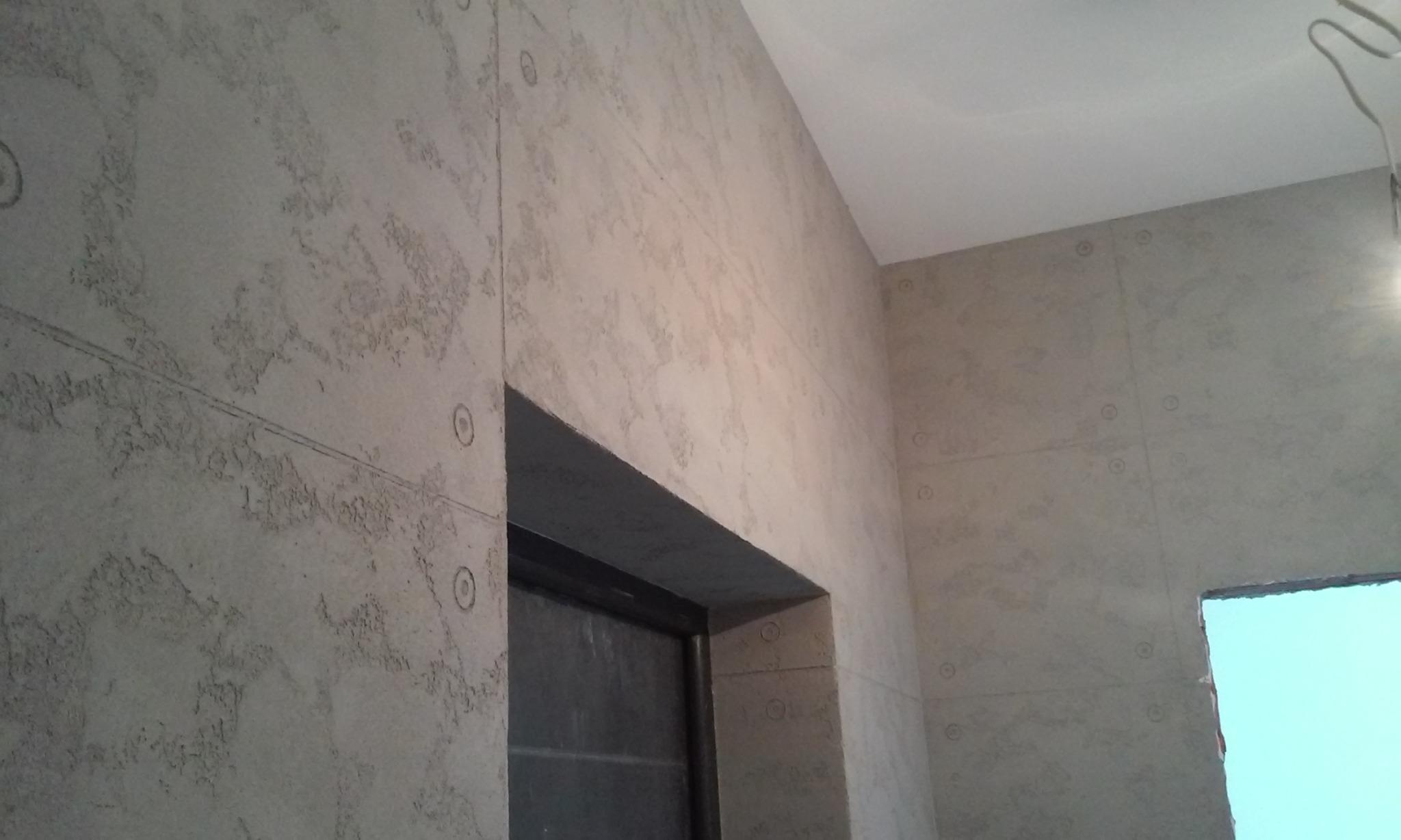 Wykończona ściana wewnętrzna z dekoracyjną fakturą i zaznaczonymi liniami podziału na panele, widoczne detale wykończenia ościeżnicy drzwiowej i fragment sufitu.