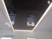 Błyszczący, czarny sufit napinany z dwoma małymi oknami dachowymi, oświetlony listwami LED po obwodzie, widok z dołu.