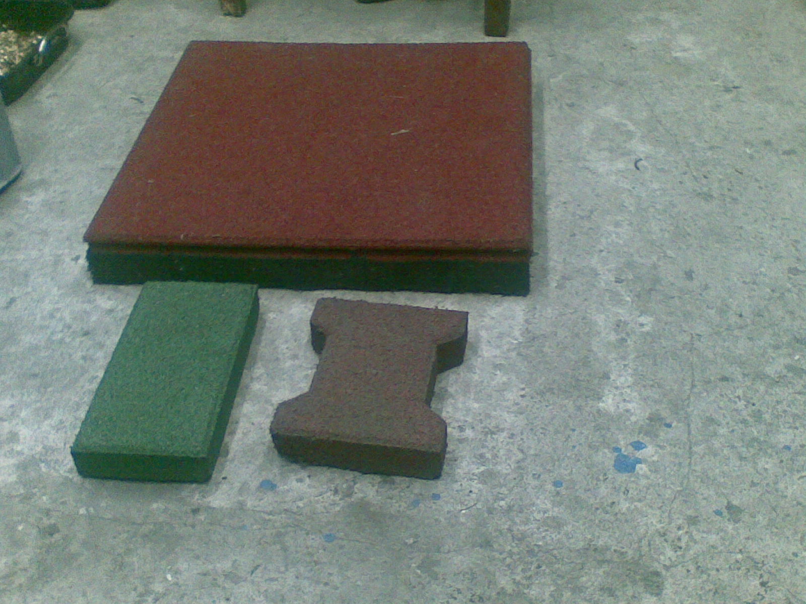 Gumowa kostka brukowa w kolorach: czerwonym, zielonym i brązowym leży na szarej betonowej posadzce.