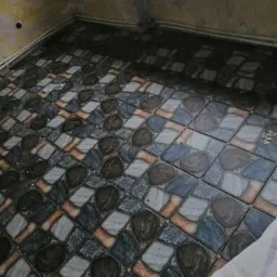 Ułożona podłoga z mozaiki w odcieniach szarości, brązu i błękitu w surowym, niedokończonym pomieszczeniu; widoczne niedoskonałości na ścianach.