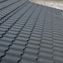 Nowy, ciemnoszary dach z blachodachówki modułowej, częściowo ukończony, z widoczną konstrukcją drewnianą i ośnieżonym terenem w tle.