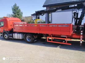 Czerwona ciężarówka z zamontowanym dźwigiem HMB 102 na tle budynku mieszkalnego z ciemną dachówką.