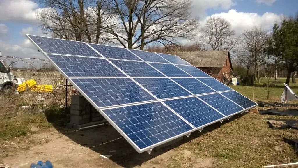 Instalacja paneli słonecznych na gruncie, widoczne betonowe bloczki jako podstawa, w tle budynek gospodarczy i częściowo widoczny samochód dostawczy