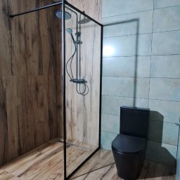 Bogdan Bróg - Nowoczesna łazienka z kabiną prysznicową typu walk-in z czarną ramą i czarną toaletą. Płytki imitujące drewno na podłodze i ścianie. Akcent turkusowych płytek.