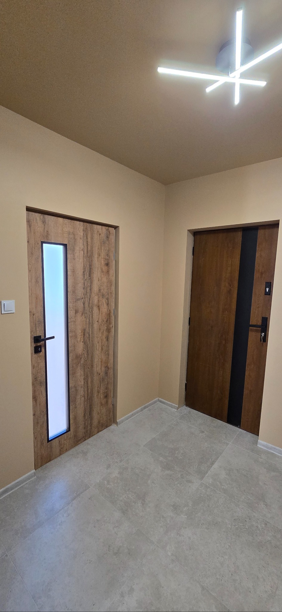 Dwa różne modele drzwi wewnętrznych z ościeżnicami, zamontowane w jasnym korytarzu z szarą podłogą z płytek. Jeden model z przeszkleniem.