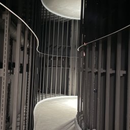 Gr Golden Renovations - Wnętrze w trakcie wykończenia: zakrzywiony korytarz z metalową konstrukcją, szare ściany i podłoga, oświetlenie górne. Widok z dołu, surowy industrialny styl.