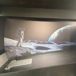 Gr Golden Renovations - Nowoczesne wykończenie wnętrza z fototapetą przedstawiającą astronautę na Księżycu i Ziemię w tle. Minimalistyczny design, ciemna kolorystyka, oświetlenie LED.