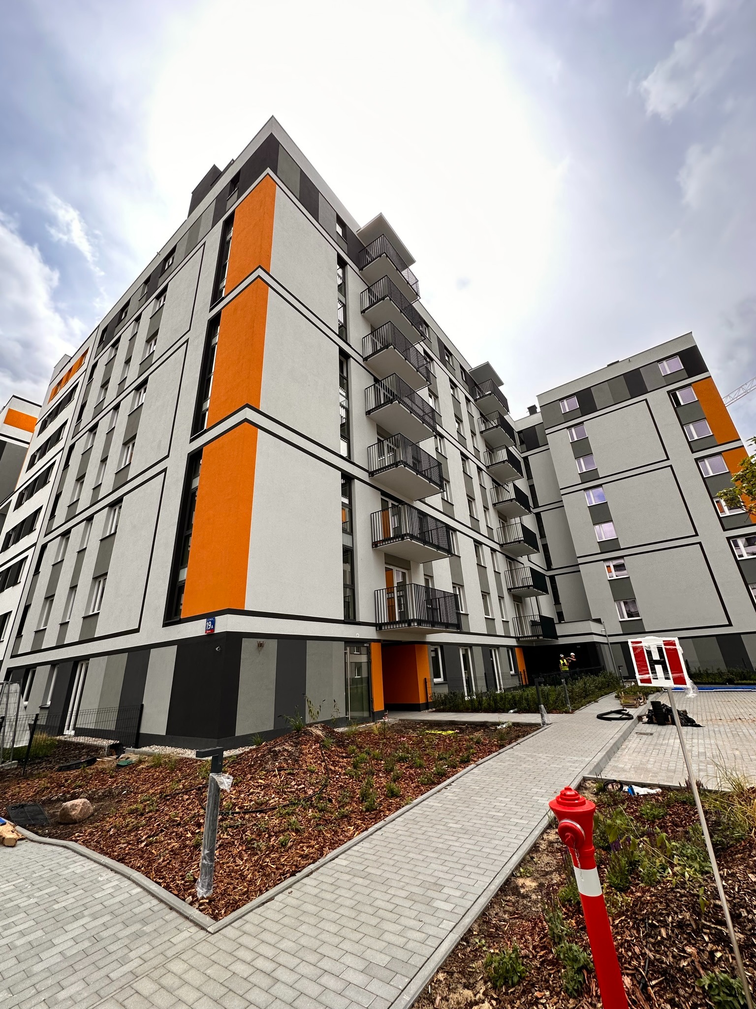 Nowoczesny budynek wielorodzinny z balkonami, świeżo po remoncie elewacji. Widoczne detale architektoniczne i nowa kolorystyka. Ujęcie z dołu podkreśla wysokość budynku.