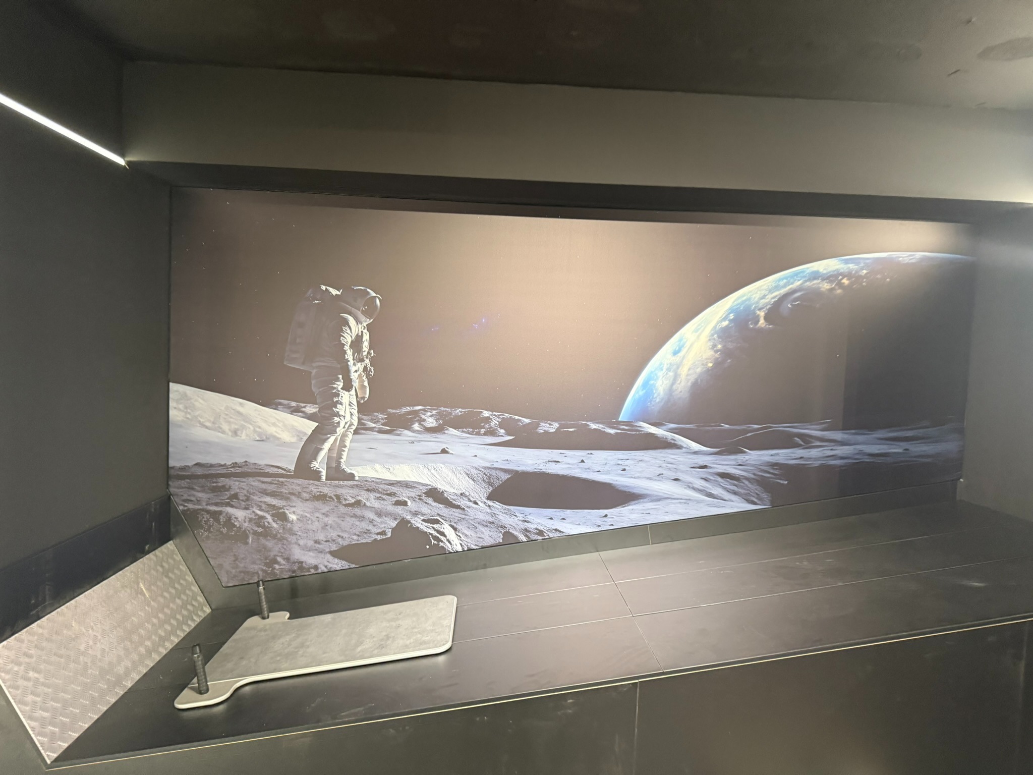 Nowoczesne wykończenie wnętrza z fototapetą przedstawiającą astronautę na Księżycu i Ziemię w tle. Minimalistyczny design, ciemna kolorystyka, oświetlenie LED.