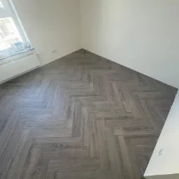 Ułożona w jodełkę, szara, panelowa podłoga w pokoju w Piasecznie, widok z góry.